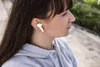 A woman wearing white earbuds outdoors. Produktbild-Vorschau