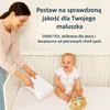 A mother placing items in a crib for a smiling baby. Podgląd zdjęcia produktu