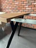 Close-up of a table's wooden tabletop and metal frame against a brick wall. Náhled obrázku produktu