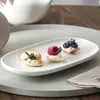 Three small tarts with fruit and cream on a white oval platter, which is on a larger gray platter. Náhled obrázku produktu