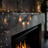 String lights draped over a fireplace mantel with a fire burning below. Produktbild-Vorschau