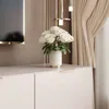 A close-up shot of a white TV lowboard with gold accents, featuring a vase of white roses. Voir les images du produit