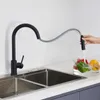 A person is using a black pull-down kitchen faucet to rinse vegetables in a sink. Produktbild-Vorschau