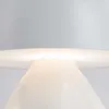 A close-up view of the top part of a white lamp, showing the light source illuminating the shade. Náhled obrázku produktu