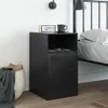 A black bedside table with a digital clock and a mug on top, next to a bed. Produktbild-Vorschau