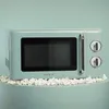 A retro-style microwave oven is displayed on a light teal surface, surrounded by popcorn. Produktbild-Vorschau