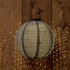 A black paper lantern with a decorative pattern is hanging against a wooden wall, casting intricate shadows. Voir les images du produit