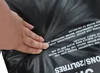 A hand is pressing on a black camping shower bag with white text printed on it. Náhled obrázku produktu