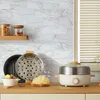 Weißer elektrischer Topf mit Edelstahl-Dämpfeinsatz und Glasdeckel auf einer Holztheke, neben einer Schüssel mit Essen Produktbild-Vorschau