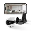 A companion robot and its charging dock are displayed in front of a smartphone screen showing a live feed of a living room. Produktbild-Vorschau