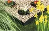 A garden scene with a black metal lawn edge separating gravel and grass, featuring potted flowers and daffodils. Produktbild-Vorschau