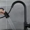 A hand is holding a black pull-down kitchen faucet spray head, with water spraying out. Produktbild-Vorschau