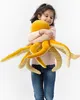 A young girl hugs a large yellow plush octopus toy. Anteprima dell’immagine prodotto