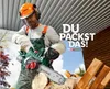 A man wearing safety gear is using a cordless chainsaw to cut wood. Produktbild-Vorschau