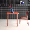 A terracotta colored table and chair set against a black tiled wall. Anteprima dell’immagine prodotto