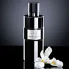 A black and white bottle of Korloff Paris Iris Doré Eau de Parfum is displayed on a reflective black surface with a gradient gray background. A white iris flower is placed to the right of the bottle. Produktbild-Vorschau