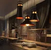 A dimly lit restaurant or lounge area with wooden furniture and decorative wall art, featuring three black pendant lights with gold accents hanging from the ceiling. Náhled obrázku produktu