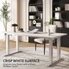 A modern white standing desk in a bright home office setting, with a plant and bookshelf in the background. Voir les images du produit