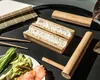 A sushi-making set with rice, chopsticks, salmon, avocado, and cucumber on a black tray. Náhľad obrázku produktu
