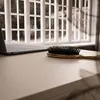 A laptop and a hairbrush are placed on a desk in front of a window. Produktbild-Vorschau