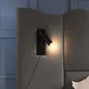 A close-up of a wall-mounted reading lamp attached to a grey upholstered headboard. Produktbild-Vorschau