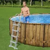 A man is standing next to an above-ground swimming pool, holding onto the ladder. Produktbild-Vorschau