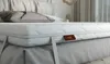 A close-up view of a white topper mattress with gray straps and a brown label. Produktbild-Vorschau