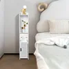 A narrow white storage cabinet is placed next to a bed with a fluffy white headboard. Produktbild-Vorschau