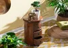 A wooden nightstand with an elephant figurine and a potted plant on top, placed on a rug next to a large plant and a floor cushion. Voir les images du produit