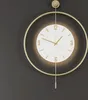 A modern wall clock with a gold metal frame and a white face, hanging against a dark gray wall. Náhľad obrázku produktu