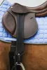 A close-up view of a brown leather saddle on a blue saddle pad, with a black stirrup strap visible. Produktbild-Vorschau