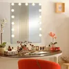 A vanity table with a lighted makeup mirror, makeup brushes, and other beauty products. Podgląd zdjęcia produktu