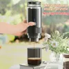 A hand holding a portable espresso machine, with coffee brewing into a cup, set against a blurred outdoor background with flowers. Náhled obrázku produktu