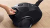A hand is shown operating a black Bosch vacuum cleaner on a wooden floor. Produktbild-Vorschau