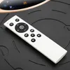 A close-up shot of a white remote control resting on a black textured surface, with a portion of a gold and black device visible in the background. Náhľad obrázku produktu