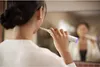 A woman brushing her teeth in front of a mirror with an electric toothbrush. Produktbild-Vorschau