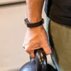 A person's arm wearing a fitness tracker is holding a kettlebell. Produktbild-Vorschau