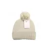 A cream-colored knitted beanie with a pom-pom on top, featuring a Nike tag attached. Voir les images du produit