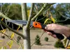 A person's hand is holding a folding saw and cutting a tree branch. Produktbild-Vorschau