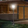 A solar-powered garden lantern illuminates a yard at dusk, with a wooden fence and garage doors in the background. Produktbild-Vorschau