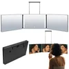 A tri-fold makeup mirror with LED lights is shown in two configurations: one suspended from above, and another being used by a person. A folded version of the mirror is also displayed. Produktbild-Vorschau