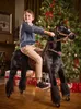 A young boy is riding a black mechanical horse in front of a decorated Christmas tree and presents. Anteprima dell’immagine prodotto