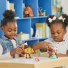 Two young girls playing with action figures on a table in front of a blue bookshelf. Podgląd zdjęcia produktu