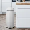 A cream-colored trash can with a black rim and pedal is shown in a modern kitchen setting. Produktbild-Vorschau
