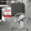 A chrome floor fan is shown in a modern living room setting, with a sofa and a decorative award in the foreground. Produktbild-Vorschau