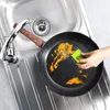 A hand is cleaning a frying pan in a sink with a sponge. Anteprima dell’immagine prodotto