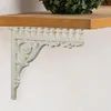 A white cast iron shelf bracket with ornate detailing is attached to a white wall, supporting a wooden shelf. Náhľad obrázku produktu