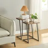 Two nesting side tables with wooden tops and black metal legs are placed next to a sofa in a living room setting. Podgląd zdjęcia produktu