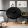 A close-up of a black foot switch for a floor lamp, with a blurred background of a modern living room. Anteprima dell’immagine prodotto