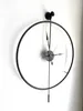 A black metal wall clock with a pendulum hangs on a white wall. Voir les images du produit